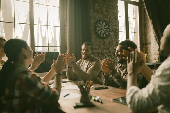 Coworkers sitting around a table and clapping for one person